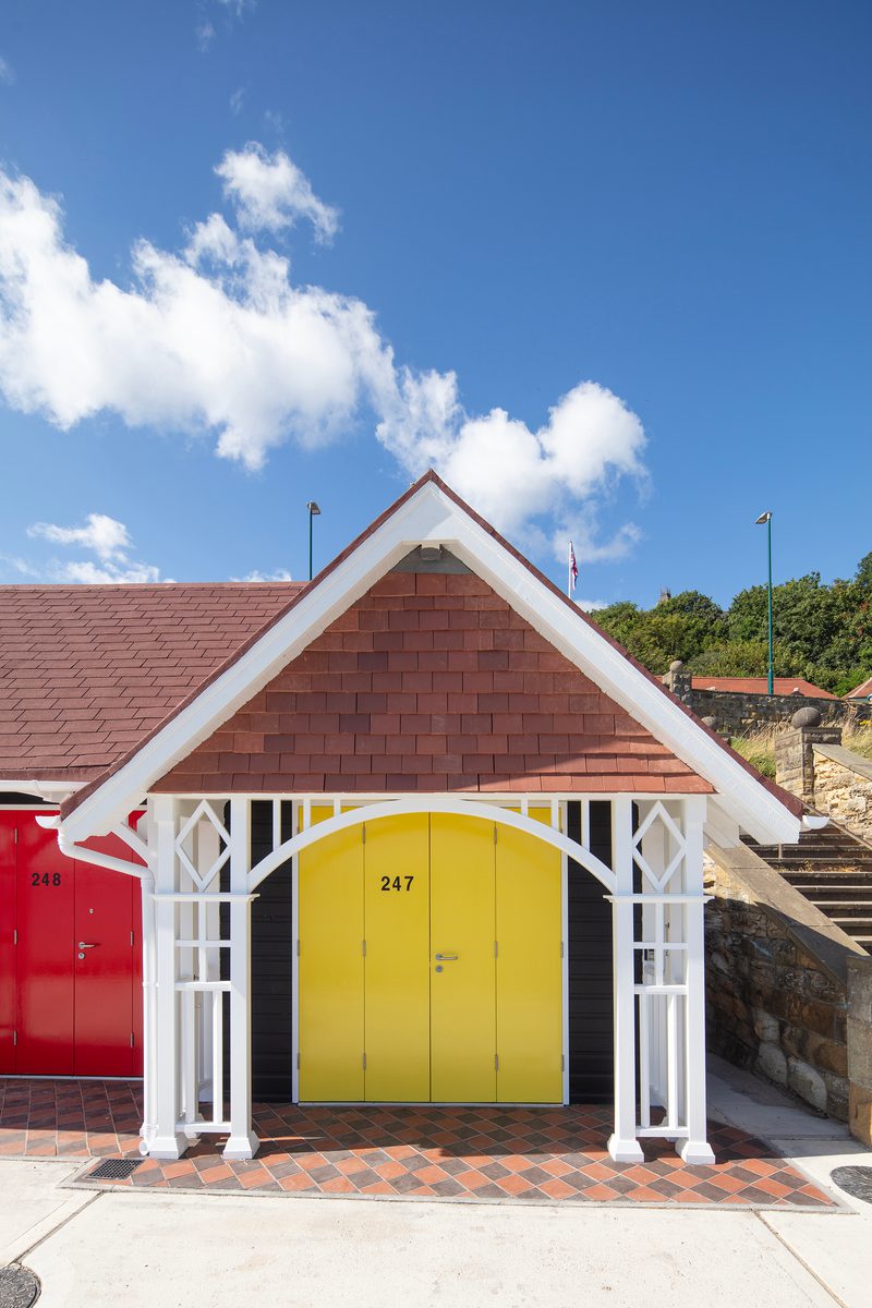 A front view of one of the beach chalets on Scarborough's South Cliff, with a bright yellow door, decorative wooden features and floor tiles,