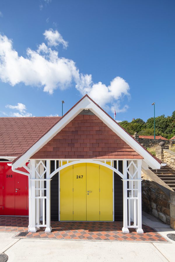A front view of one of the beach chalets on Scarborough's South Cliff, with a bright yellow door, decorative wooden features and floor tiles,