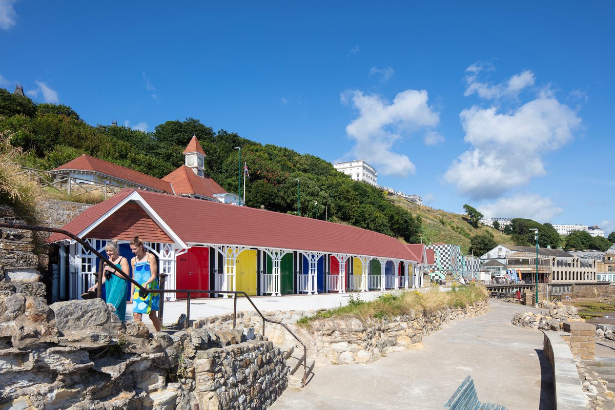 Beachgoers in front of the rebuilt colourful beach chalets on Scarborough's South Cliff, showing their cliffside, beach front location.