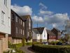 Some of the different coloured, wooden clad houses with gabled rooves of varying heights, set around a landscaped, green public space within the Fishing Village part of St Mary's Island masterplan.