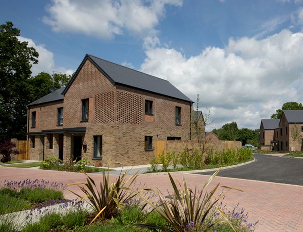 Exterior of one house in the Passivhaus residential development, The Pheasantry, surrounded by planting and space for parking.