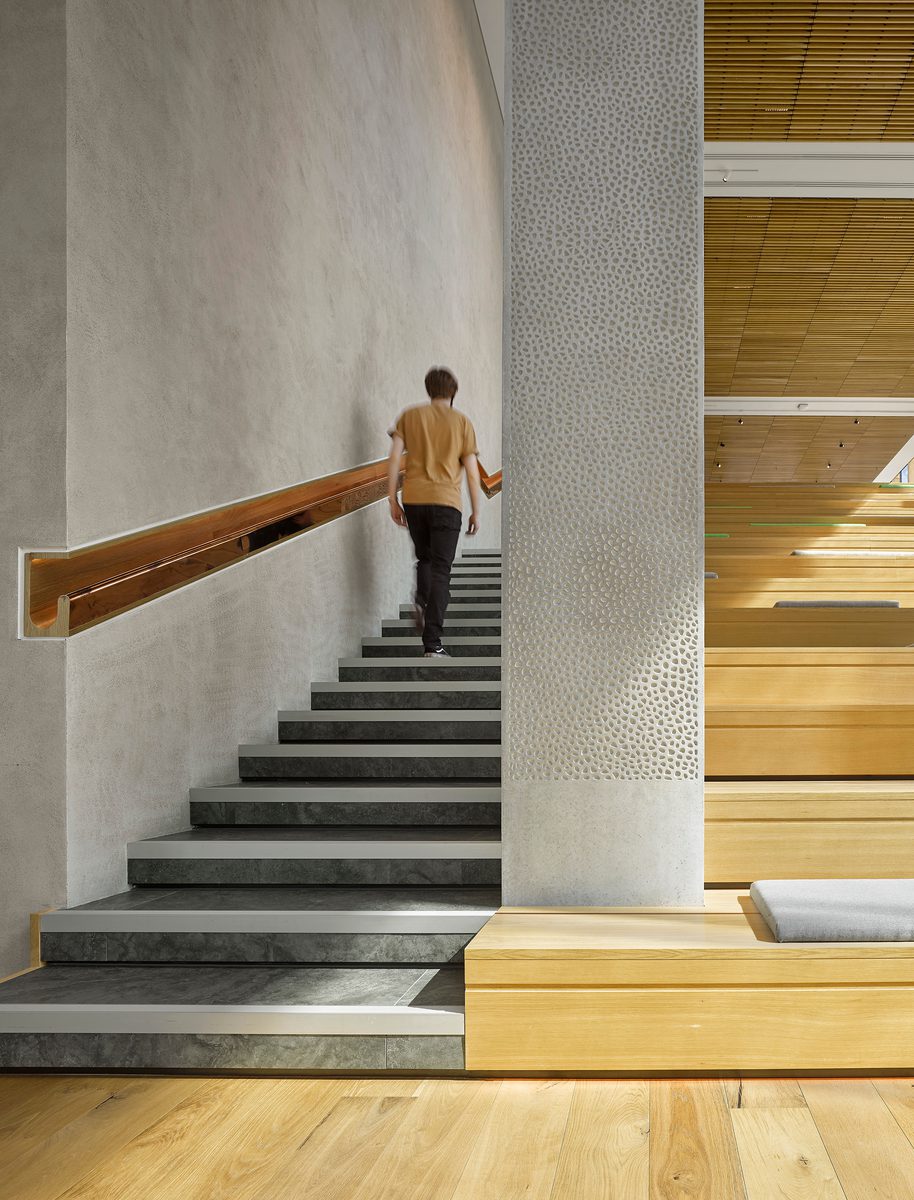 Somebody walking upstairs adjacent on the wooden to the Spanish steps in a shared space within the Spine, with recessed wooden handrail.