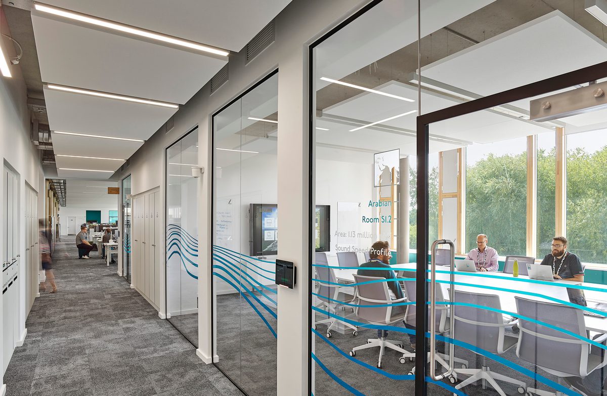People sat in a meeting room within the UK Hydrographic Office, with floor to ceiling windows and bespoke wall graphics.
