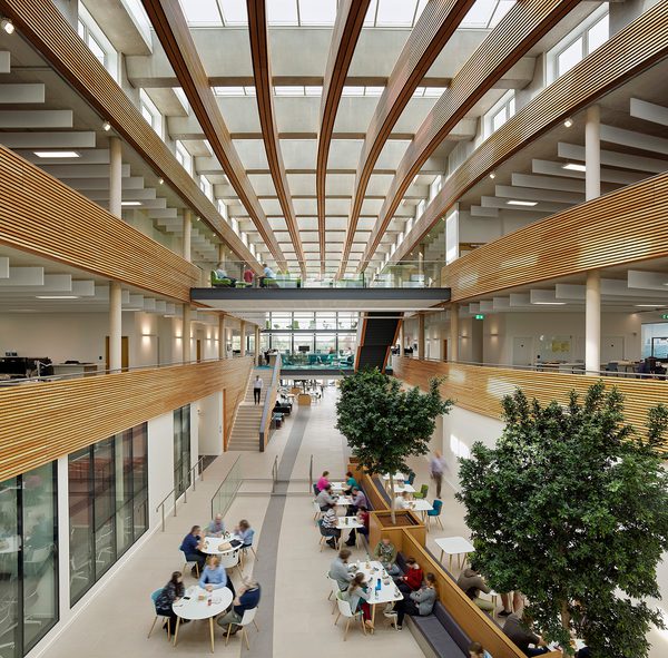 The bright large open atrium of the UK Hydrographic Office with a variety of workspaces, indoor biophilic planting, innovative wooden ceiling structure and glazed roof.