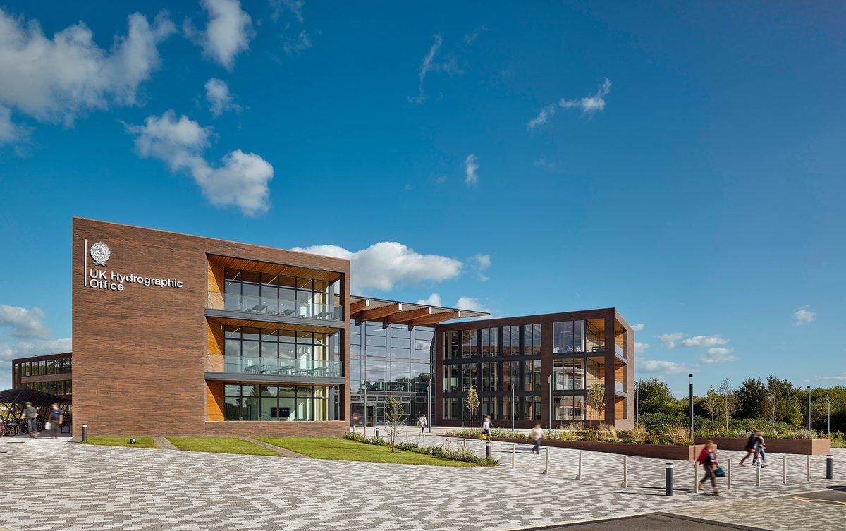 The exterior front entrance of the UK Hydrographic Office, showing the high level of glazing, bicycle storage facilities and planting surrounding the building.