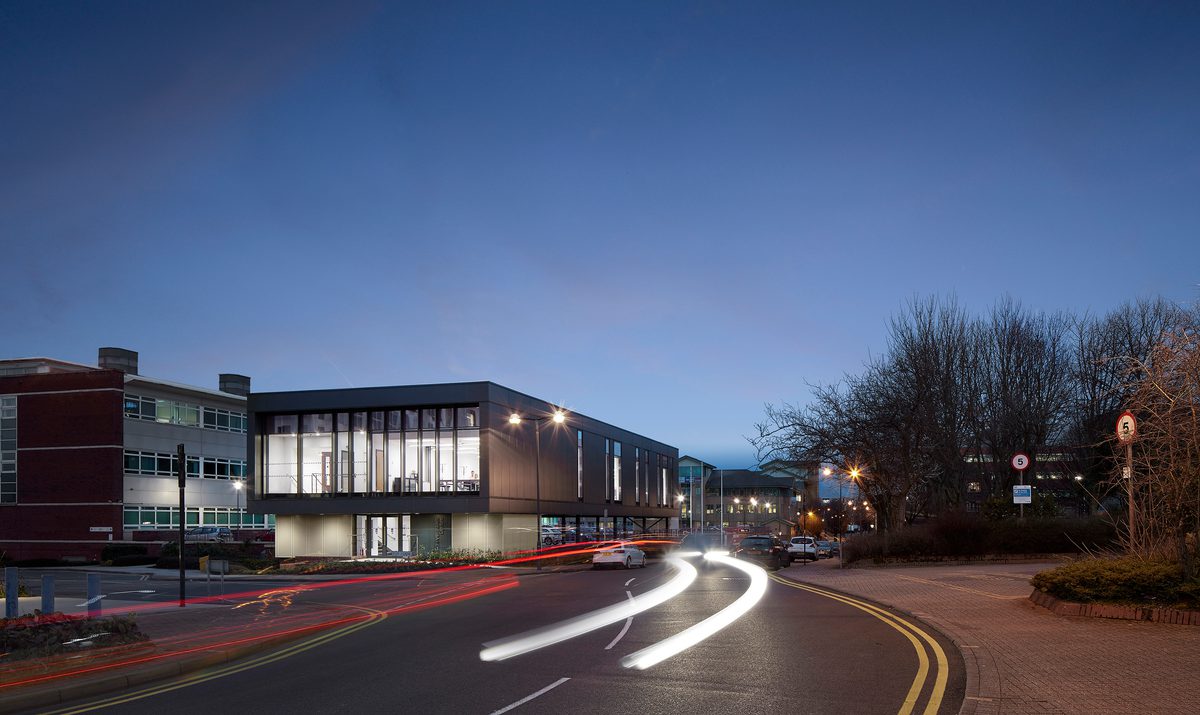 The exterior of the entirety of the Universities Centre at dusk, showing its floor to ceiling windows and prominent location.