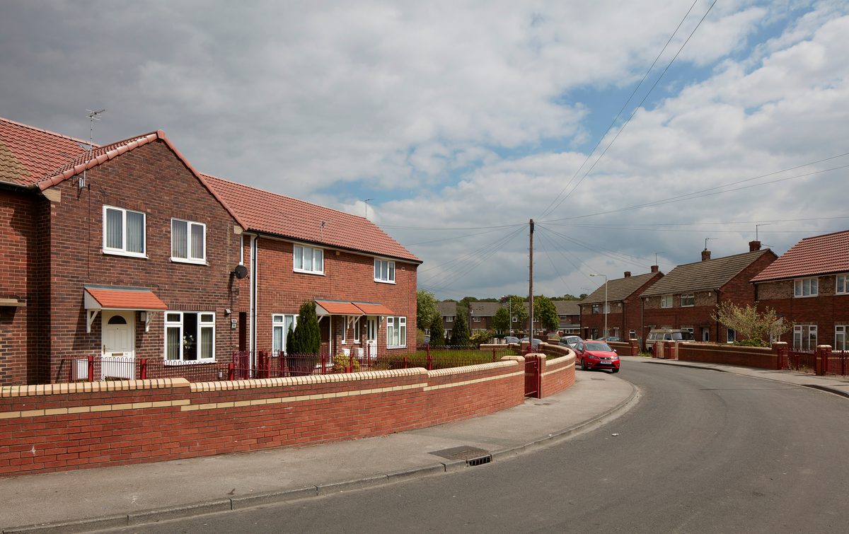 A redbrick house exterior in a residential development for Vico Homes, with other houses surrounding.