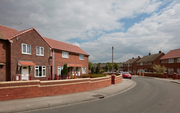 A redbrick house exterior in a residential development for Vico Homes, with other houses surrounding.