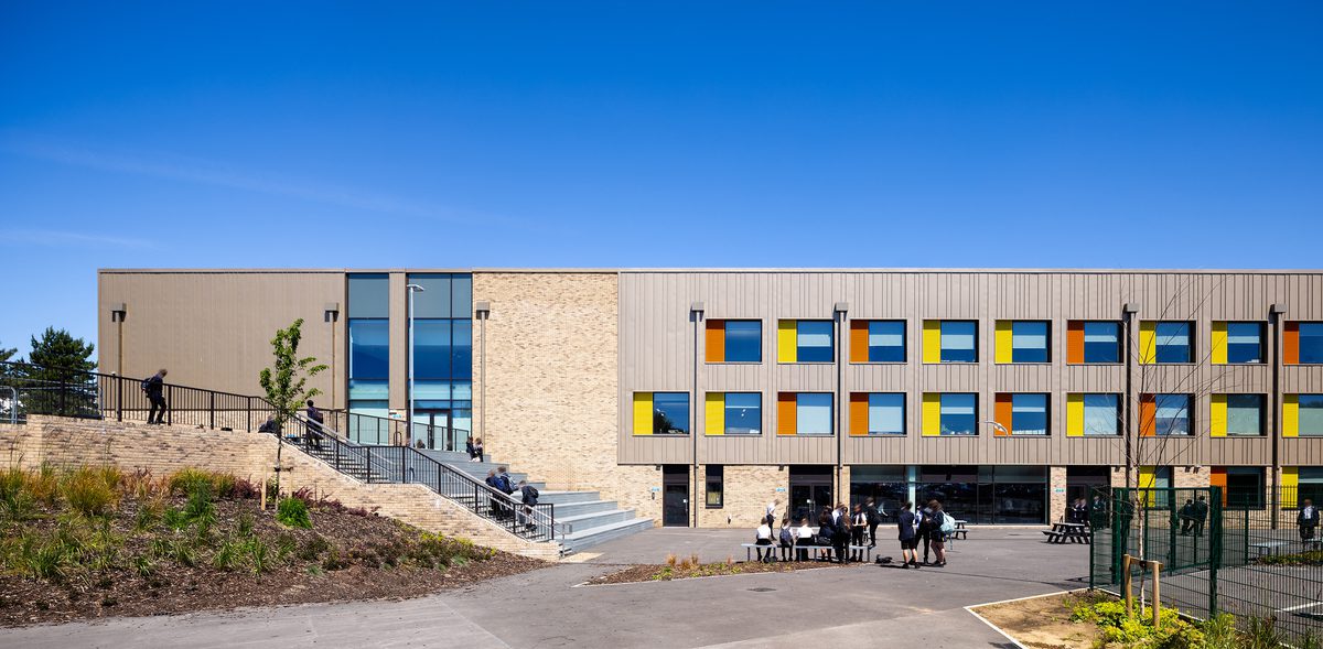 Students using the outdoor space surrounding Winterstoke hundred Academy, showing one side of the building with colourful facade detailing and surrounded by greenery.