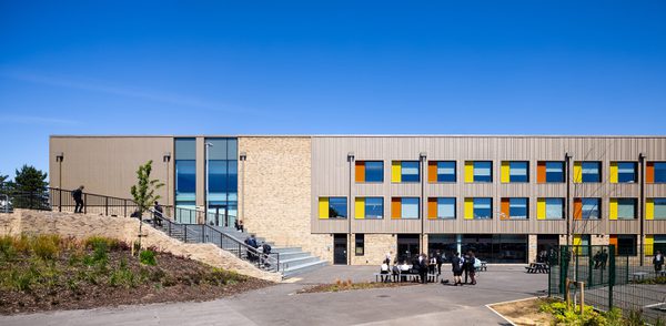 Students using the outdoor space surrounding Winterstoke hundred Academy, showing one side of the building with colourful facade detailing and surrounded by greenery.