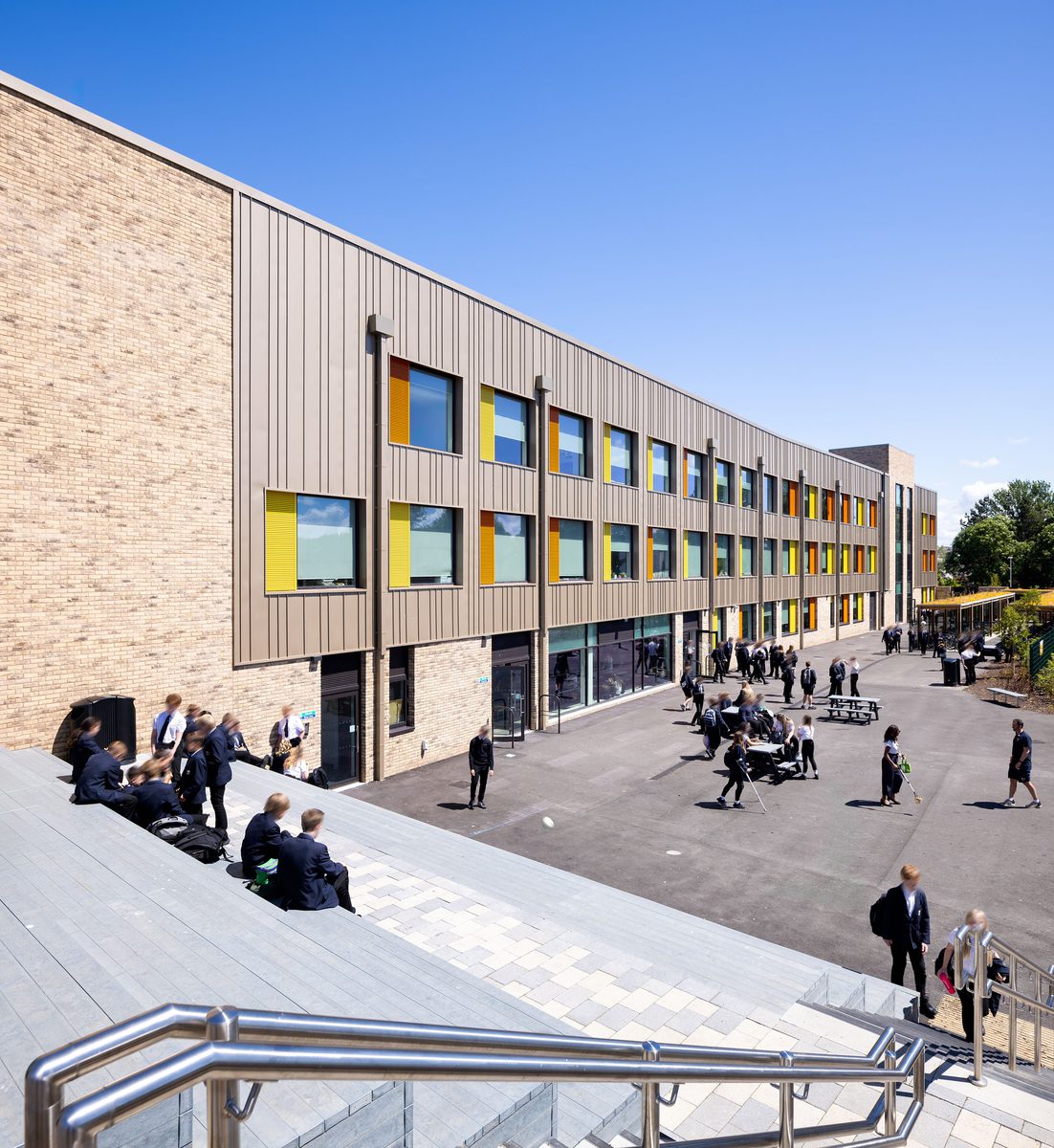 Students using the outdoor space surrounding the Winterstoke Hundred Academy, showing the variety of seating options and colourful facade details.