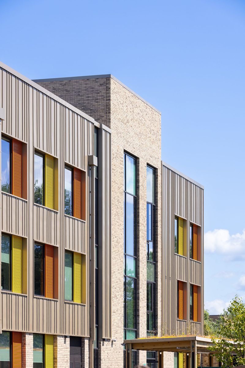 An exterior detail shot of the upper two levels of the Winterstoke Hundred Academy, with grey facade and orange and yellow detailing.